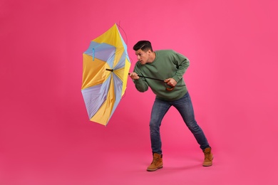 Photo of Man with umbrella caught in gust of wind on pink background
