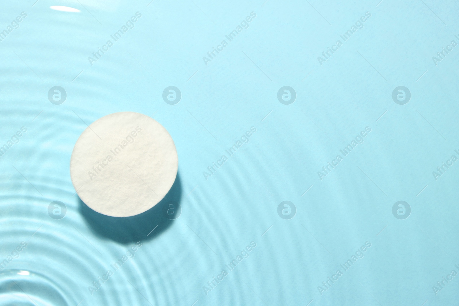 Image of Cotton pad in micellar water on light blue background, top view. Space for text