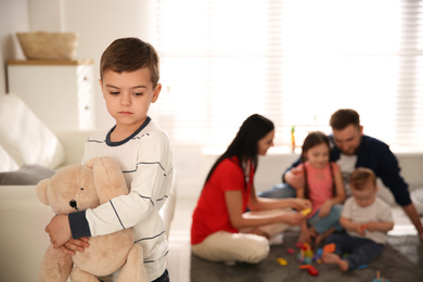 Photo of Unhappy little boy feeling jealous while parents spending time with other children at home