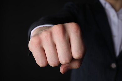 Businessman showing fist with space for tattoo on black background, closeup