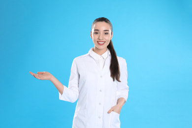 Photo of Happy young woman in lab coat on light blue background