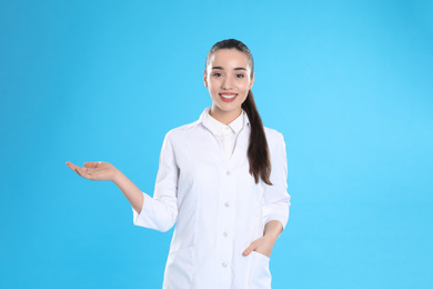 Happy young woman in lab coat on light blue background