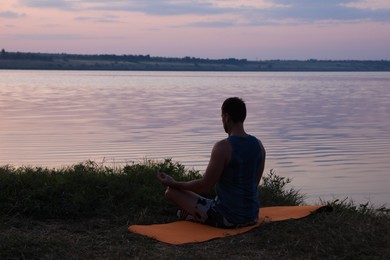 Photo of Man meditating near river in twilight, back view