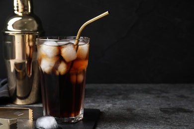 Photo of Tasty cola with ice cubes on grey table against dark background, space for text