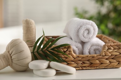 Spa composition. Towels, stones, herbal bags and palm leaves on white table indoors