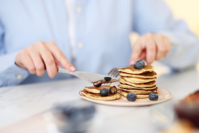 Tasty breakfast. Woman eating pancakes with blueberries at white table, closeup