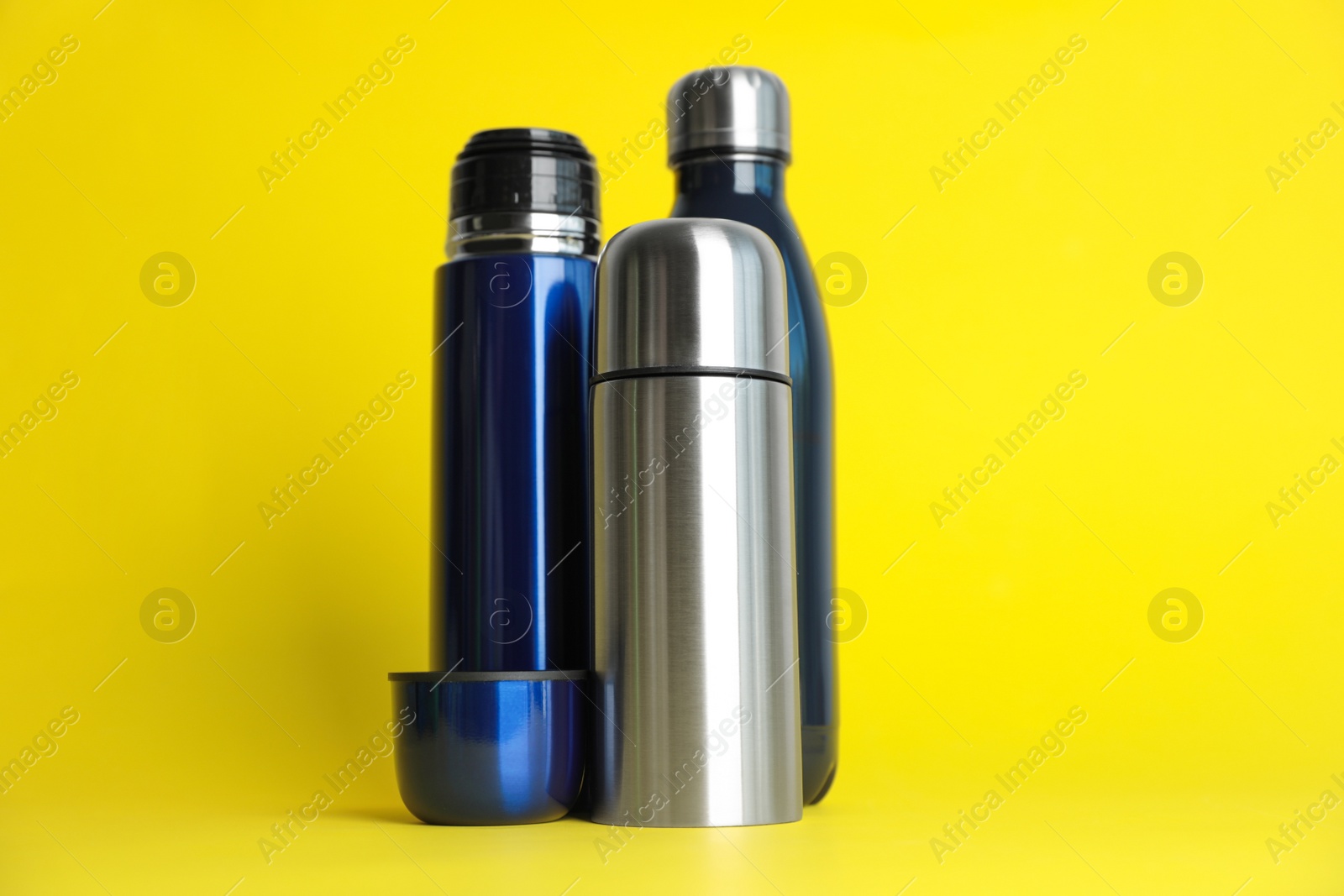 Photo of Stylish stainless thermo bottles on yellow background