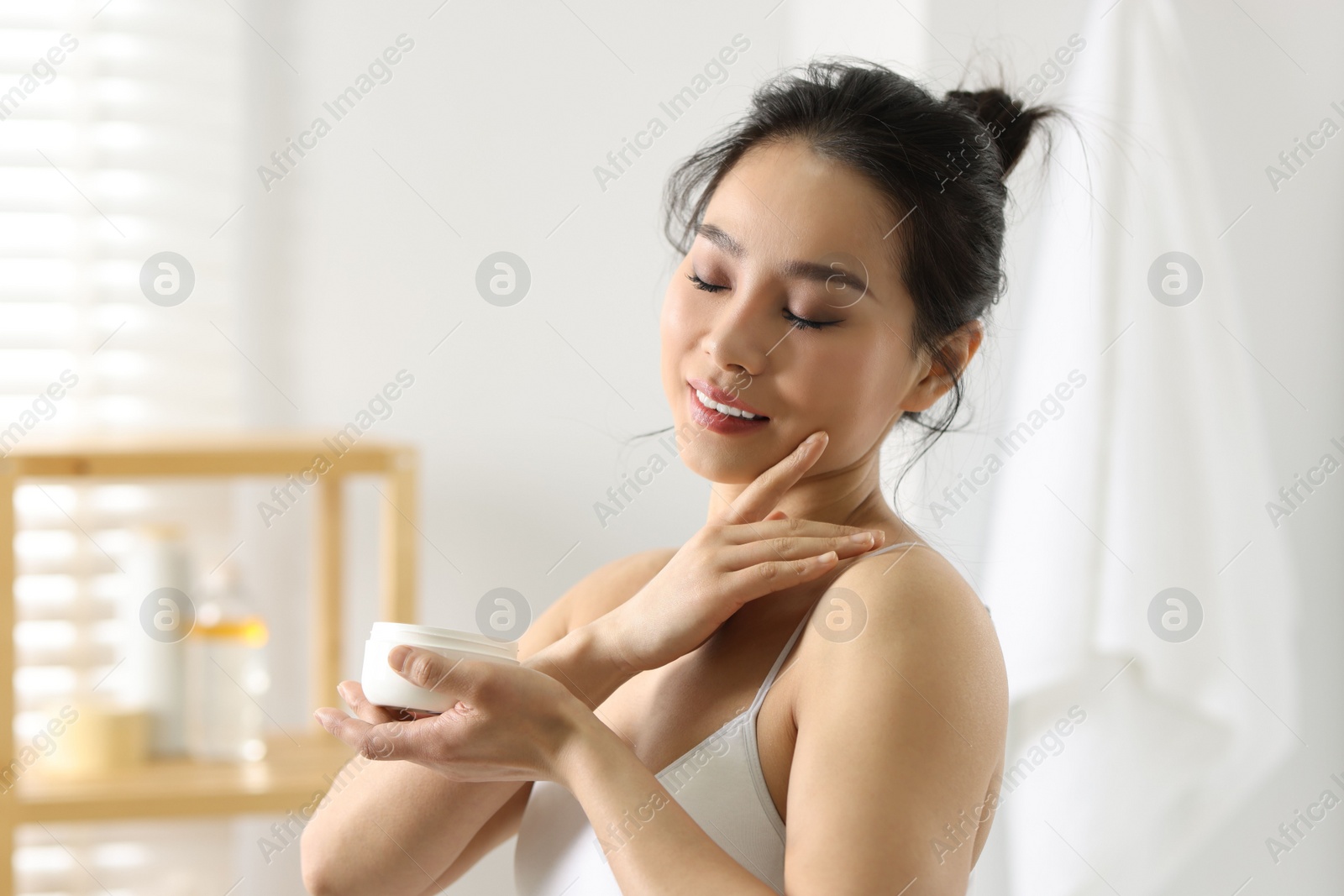 Photo of Happy woman applying body cream at home