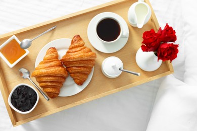 Photo of Tasty breakfast served in bed. Fresh croissants, coffee, honey and jam on wooden tray