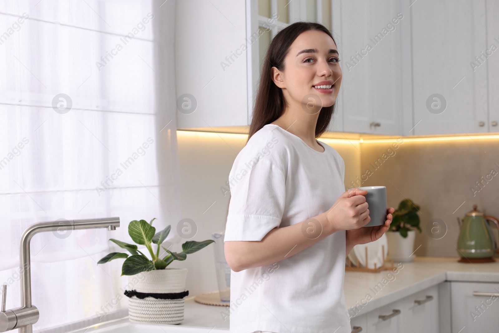 Photo of Happy woman with cup of drink in kitchen, space for text. Lazy morning