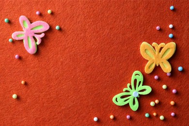 Photo of Small colorful beads and felt butterflies on red background, flat lay. Space for text