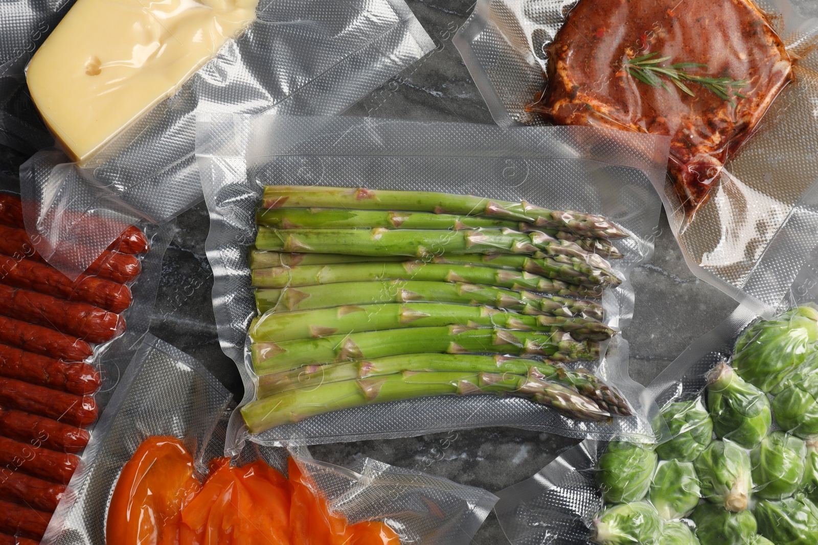 Photo of Different food products in vacuum packs on black marble table, flat lay