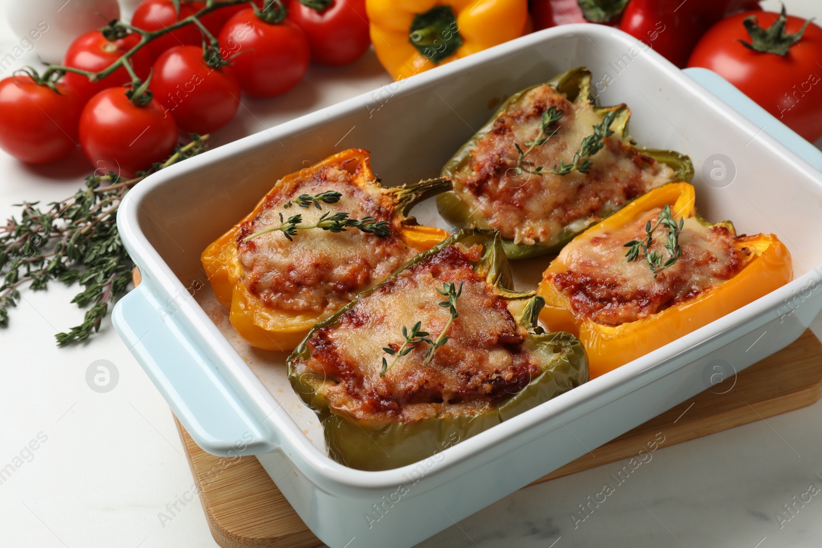 Photo of Tasty stuffed peppers in dish and ingredients on white table