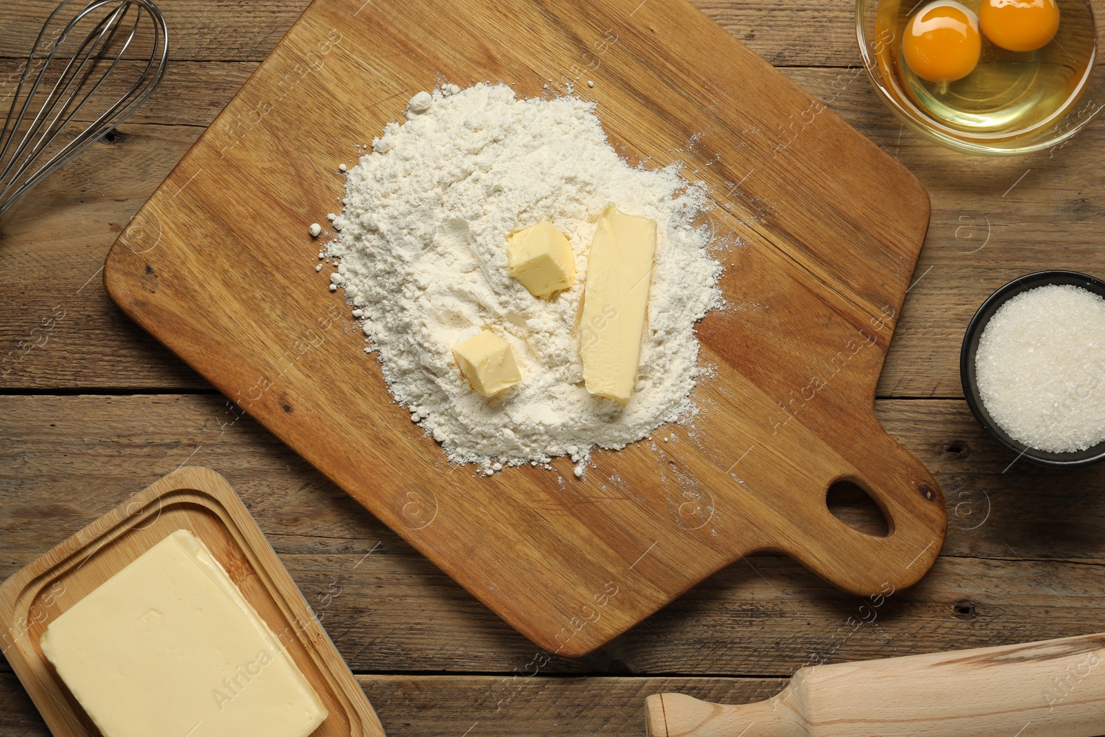 Photo of Board with fresh butter and flour on wooden table, flat lay