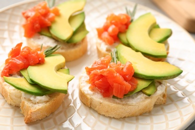 Tasty sandwiches with fresh sliced salmon fillet and avocado on plate, closeup