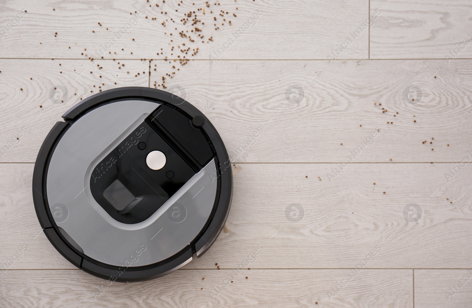 Photo of Modern robotic vacuum cleaner removing scattered buckwheat from wooden floor, top view. Space for text