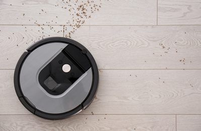 Photo of Modern robotic vacuum cleaner removing scattered buckwheat from wooden floor, top view. Space for text