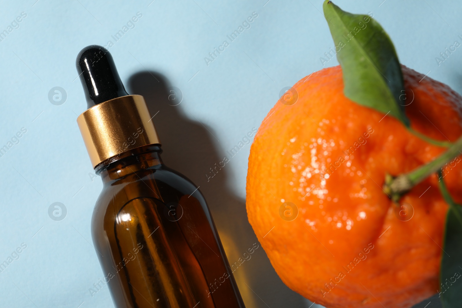 Photo of Aromatic tangerine essential oil in bottle and citrus fruit on light blue table, top view