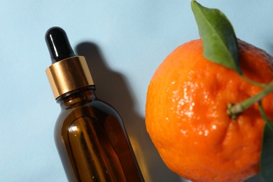 Aromatic tangerine essential oil in bottle and citrus fruit on light blue table, top view