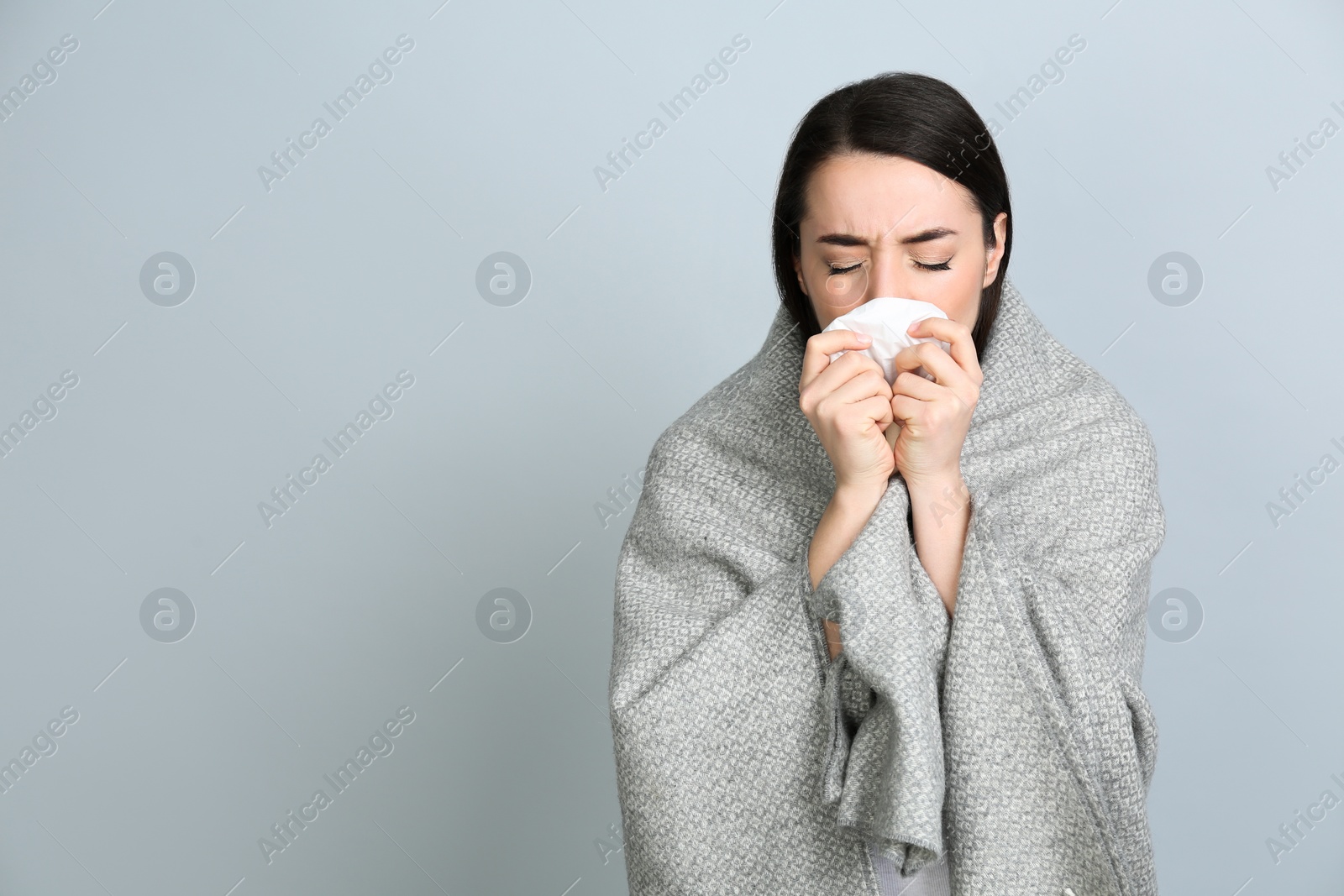 Photo of Young woman with blanket suffering from runny nose on light grey background. Space for text