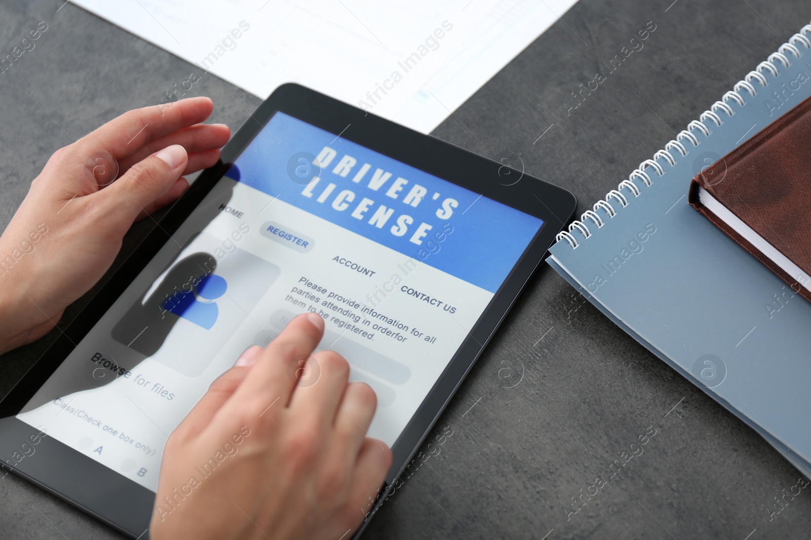 Photo of Person using tablet to fill driver's license application form at grey table, closeup