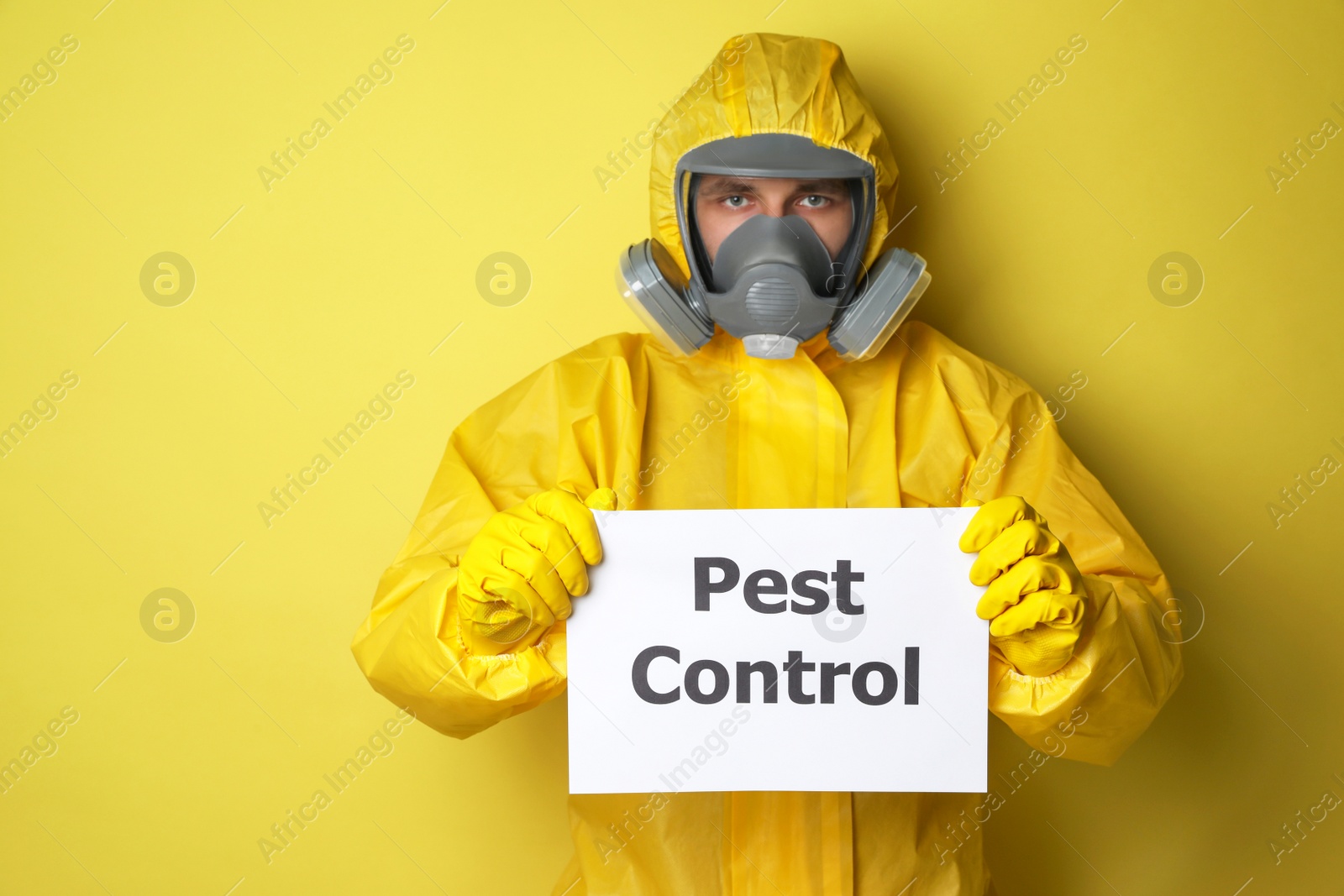 Photo of Man wearing protective suit with insecticide sprayer holding sign PEST CONTROL on yellow background