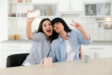 Photo of Young woman and her mature mother taking selfie at table indoors