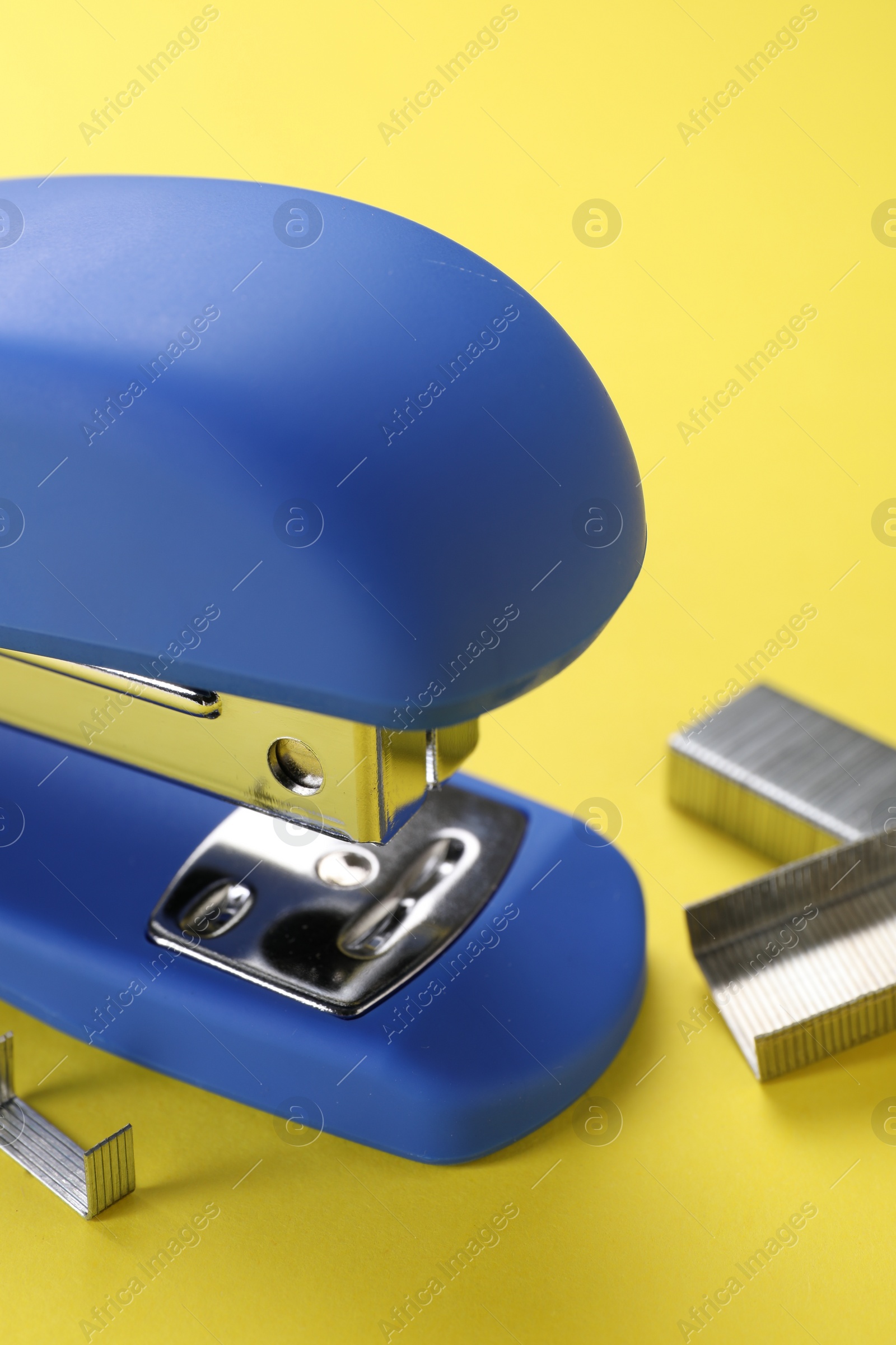 Photo of Blue stapler with staples on yellow background, closeup