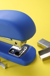 Blue stapler with staples on yellow background, closeup