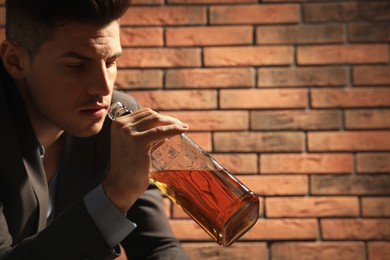 Addicted man drinking alcohol near red brick wall. Space for text