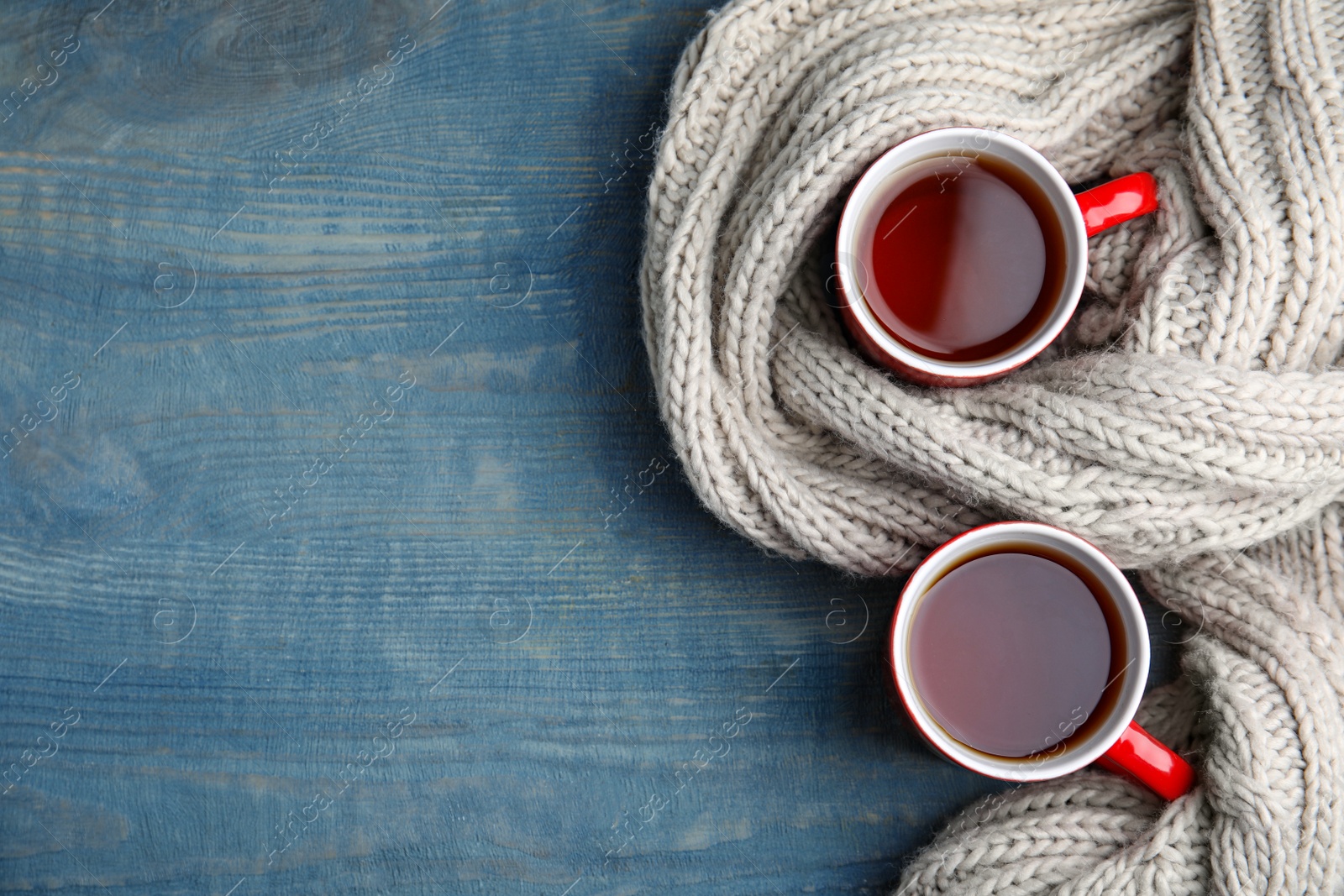 Photo of Flat lay composition cups of hot tea and knitted scarf on blue background, space for text. Winter drink