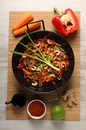 Shrimp stir fry with vegetables in wok and ingredients on wooden table, flat lay