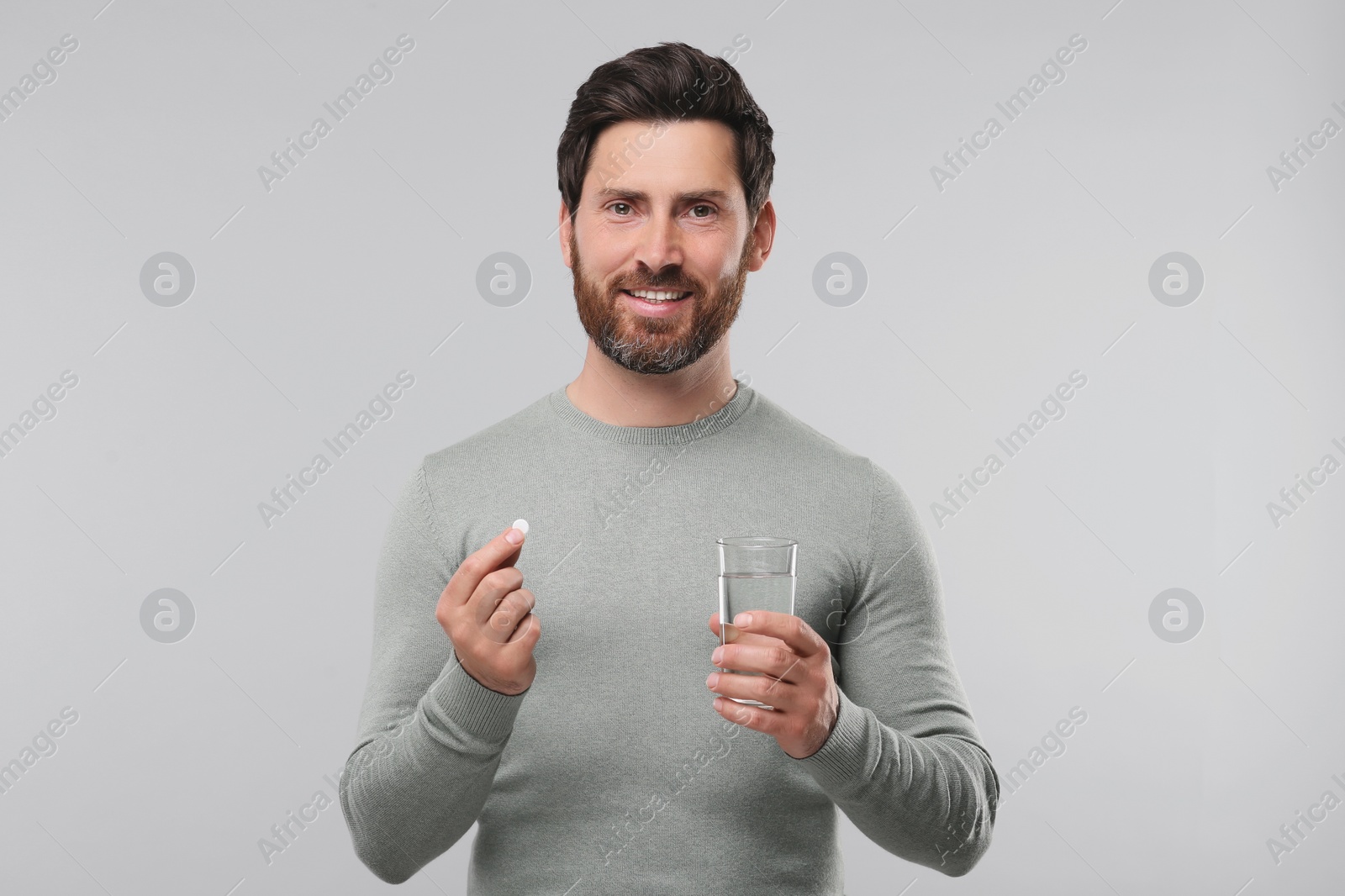 Photo of Handsome man with glass of water and pill on light grey background