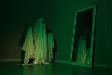 Creepy ghost. Woman covered with sheet looking at mirror in green light