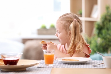 Photo of Cute little girl eating tasty toasted bread with jam at table