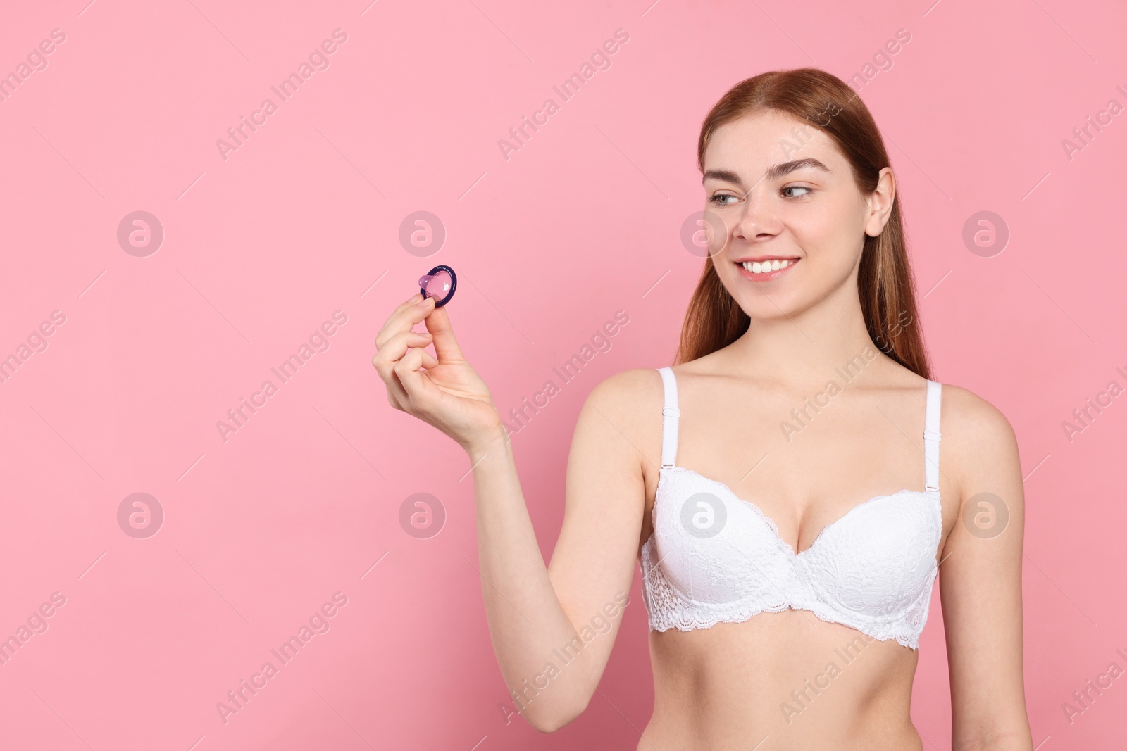 Photo of Woman in bra holding condom on pink background, space for text. Safe sex