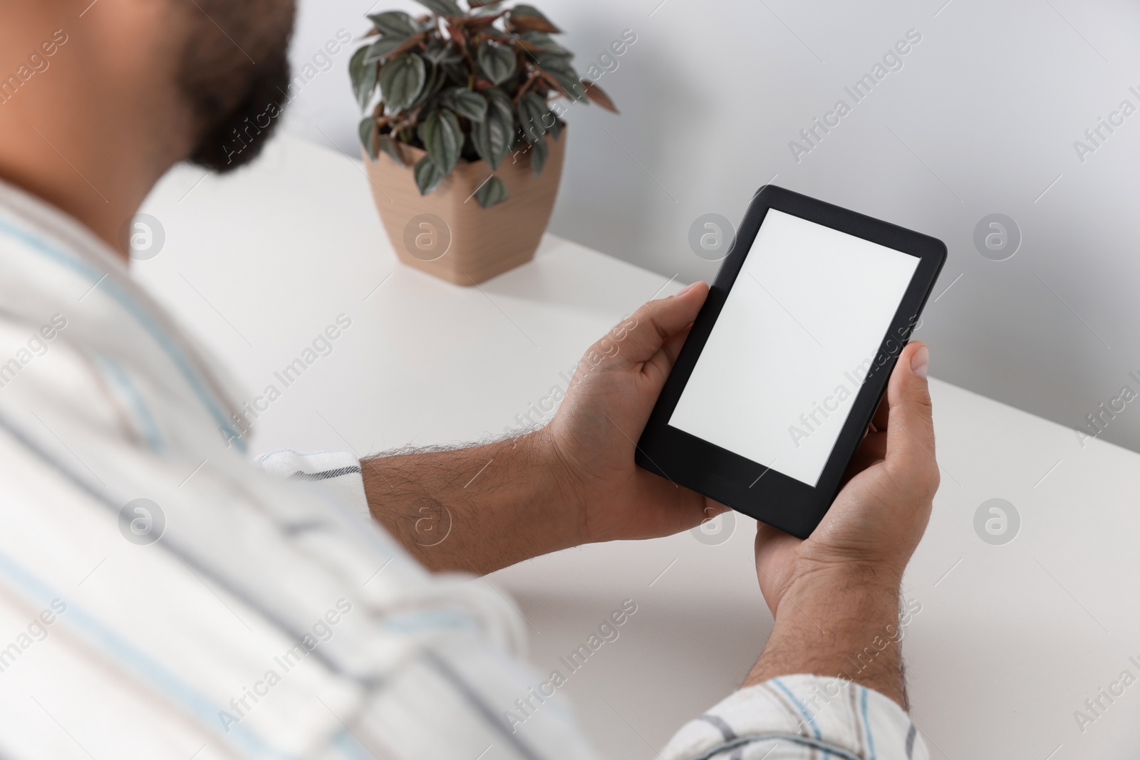 Photo of Man using e-book reader at white table indoors, closeup