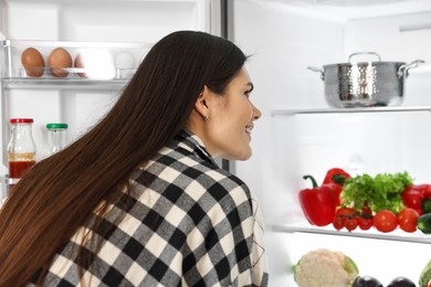 Young smiling woman looking into modern refrigerator
