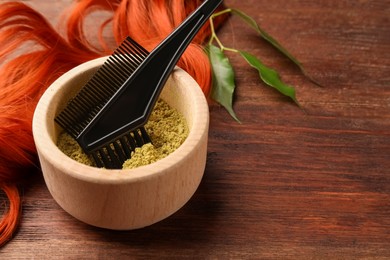 Photo of Bowl of henna powder, brush, green leaves and red strand on wooden table, closeup with space for text. Natural hair coloring