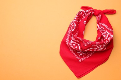 Photo of Tied red bandana with paisley pattern on orange background, top view. Space for text