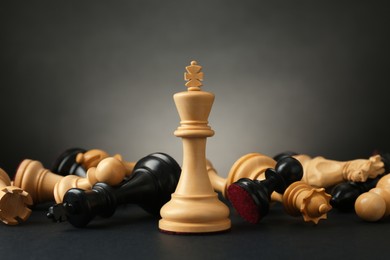Photo of White king among fallen chess pieces on dark background