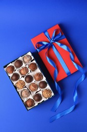 Photo of Box with delicious chocolate candies on blue background, flat lay