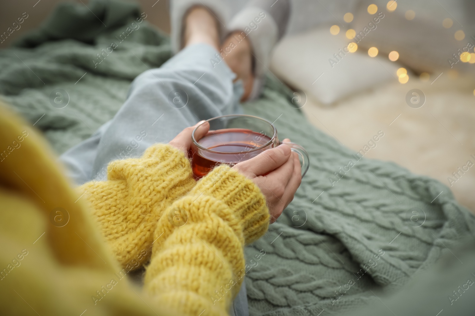 Photo of Woman with cup of tea sitting on plaid indoors, closeup