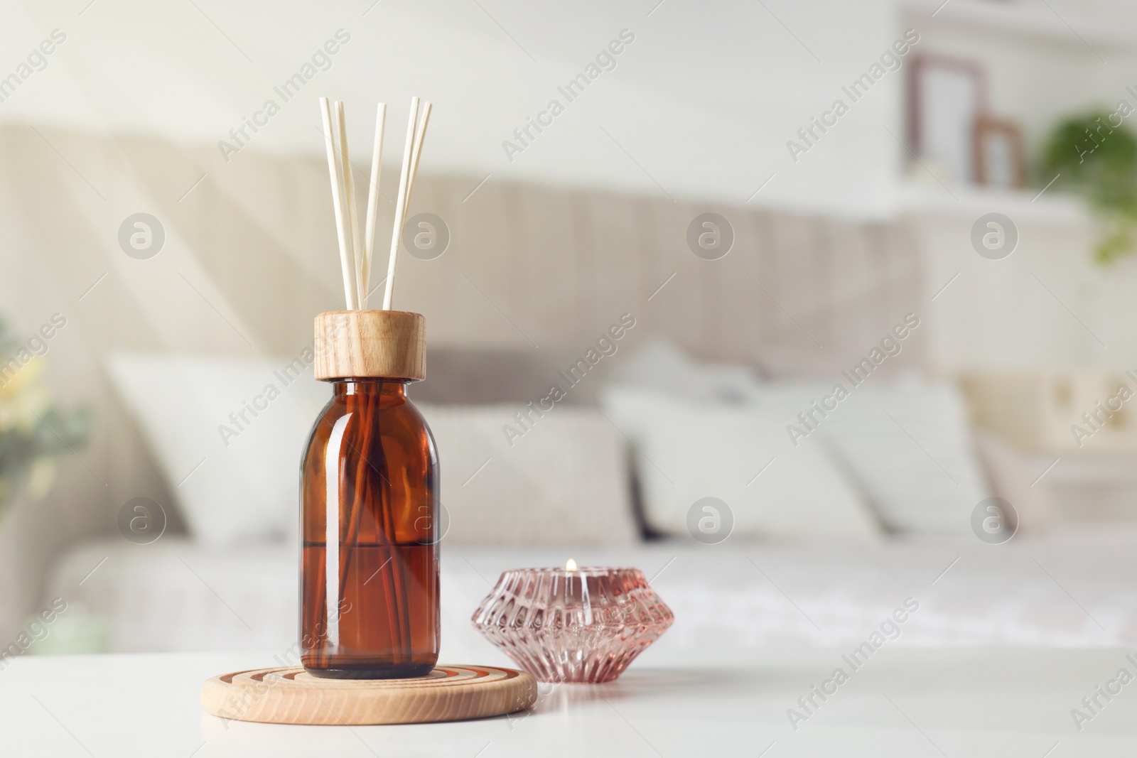 Photo of Aromatic reed air freshener and candle on white table in bedroom. Space for text