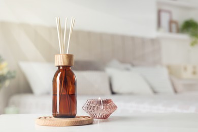 Aromatic reed air freshener and candle on white table in bedroom. Space for text