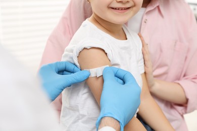 Children's hepatitis vaccination. Mother with her daughter in clinic. Doctor sticking medical plaster on little girl's arm, closeup