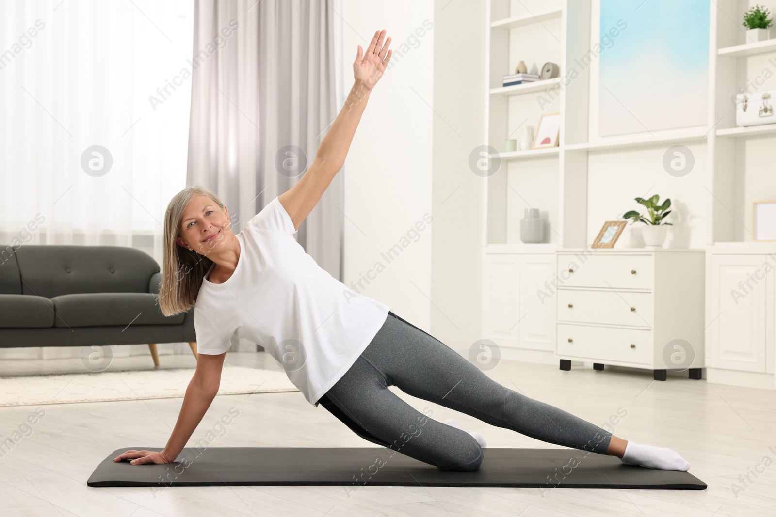 Photo of Happy senior woman practicing yoga on mat at home