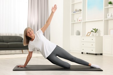 Happy senior woman practicing yoga on mat at home