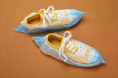 Photo of Sneakers in shoe covers on brown background, above view