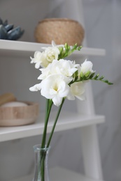 Photo of Beautiful white freesia flowers in vase on shelf indoors, closeup